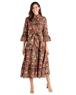 A woman modeling a long-sleeved midi dress with a high collar and a detailed paisley pattern in red, gold, and black, set against a plain white studio background.