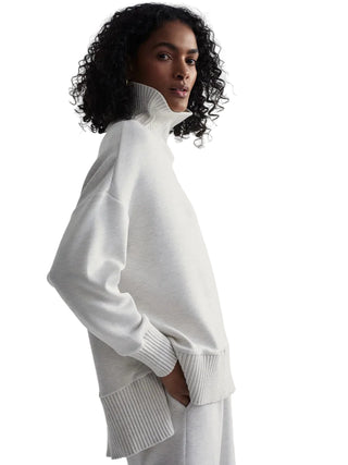 Woman wearing a white turtleneck sweater against a plain background