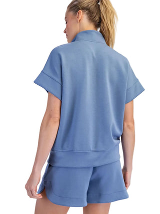 A woman shown from the back wearing a light blue short-sleeve top and matching shorts against a plain light gray studio background.