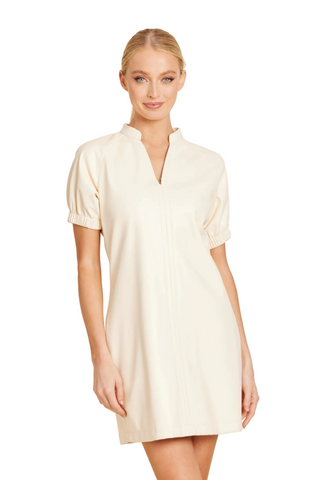 A woman modeling a short cream-colored puff-sleeve dress with a split V-neckline and front zipper, set against a solid light beige background.