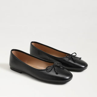 Pair of black leather flats with a bow on a light gray background