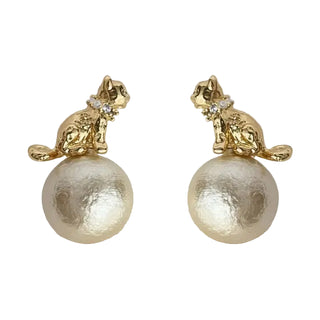 A pair of gold-tone cat stud earrings with textured cream pearl-like drops, shown on a light neutral background.