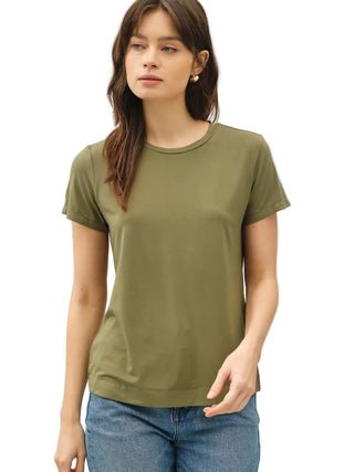 A woman wearing a short-sleeve crewneck t-shirt in olive green, paired with blue jeans, standing against a plain light gray background.