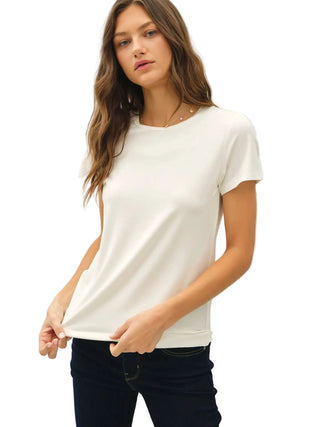 A woman modeling a short-sleeve crewneck t-shirt in off-white, paired with dark jeans, against a plain light gray background.