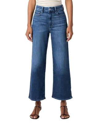 A model wearing a pair of high-waisted, wide-leg cropped blue denim jeans with a faded wash, paired with brown strappy sandals and a striped top, against a plain white studio background.