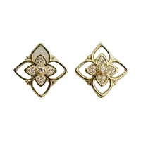A pair of gold-toned flower-shaped stud earrings with clear rhinestones and a central white stone, shown on a plain light background.