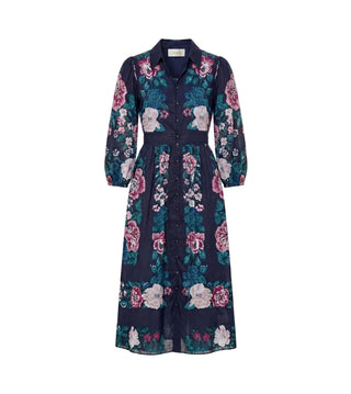 A long-sleeved midi dress with a button-up front, collar, and self-tie waist belt, featuring a dark navy blue base with a vibrant floral print in pink, green, and white, shown against a plain off-white background.