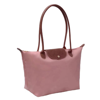 Pink handbag with brown handles on a white surface with books in the background