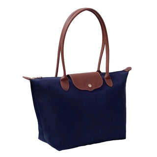 Navy handbag with brown handles and flap on a light gray surface with a white curtain background