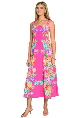 A woman modeling a sleeveless midi dress with a bright pink base and a colorful floral print, standing against a light gray studio background.