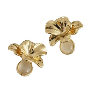A pair of gold flower-shaped stud earrings with teardrop-shaped pale cream stones, displayed on a textured white fabric background.