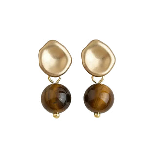 A pair of drop earrings featuring irregular, organic-shaped matte gold top halves and smooth, polished brown tiger's eye round beads hanging below, displayed on a light beige textured fabric background.