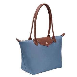 Blue handbag with brown handles and trim on a light surface with books in the background