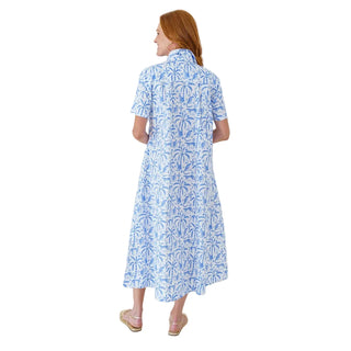Woman wearing a blue floral dress against a white brick wall.
