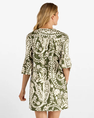 A woman viewed from the back wearing a short-sleeve, knee-length dress with a cream paisley and floral print on an olive green base, set against a plain white studio background.
