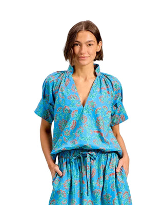 A woman modeling a matching blue patterned top and skirt set against a solid light blue background.
