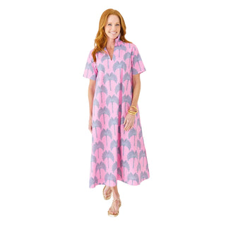 Woman wearing a pink dress with palm tree pattern against a white brick wall.