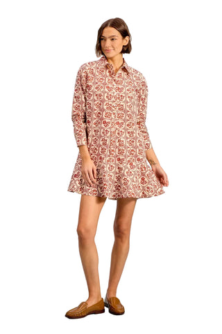 A woman modeling a long-sleeve mini shirt dress with a red and beige floral pattern, paired with brown leather loafers, against a solid light blue background.