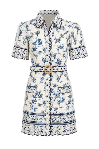 A short-sleeve collared shirt dress with a blue floral toile pattern on an off-white background, featuring a matching waist belt with a round gold-tone buckle and decorative lace trim.