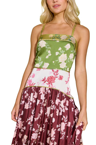 A woman wearing a sleeveless spaghetti-strap dress with a color-blocked floral design: olive green on top, white with pink flowers in the middle, and a burgundy skirt with a pink floral print, against a light green background.