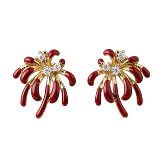 A pair of gold and red firework-shaped stud earrings with clear crystal centers, displayed on a light textured fabric background.
