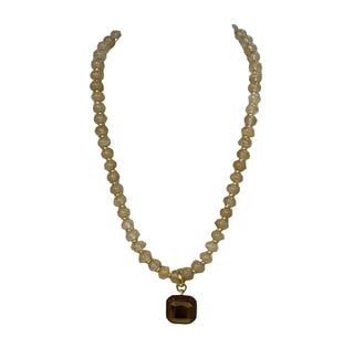 A beaded necklace with pale yellow translucent beads and a square brown pendant, displayed on a beige fabric jewelry bust against a gray background.