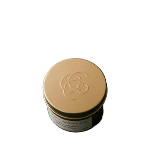 A round metal tin candle with a gold lid and a white label reading 'THE CANDLE CO' and 'SANDSTOCKED OIL', photographed on a dark charcoal background.