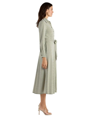 A woman modeling a long-sleeve midi shirt dress with a small-scale green and beige geometric pattern, shown in profile against a plain white studio background.
