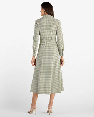 A woman viewed from the back wearing a long-sleeve midi dress with a small-scale green and beige geometric pattern, paired with beige high-heeled sandals, against a plain white studio background.
